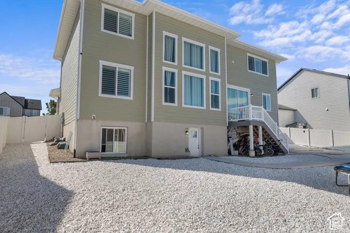 Rear exterior with light-colored siding, multiple windows, a ground-level entrance, a second-story deck with white railings, and a gravel-covered yard