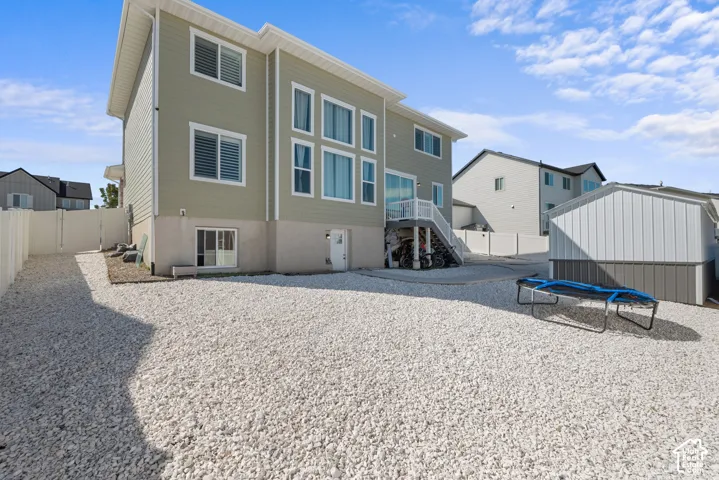 Spacious gravel yard with perimeter fencing, a detached storage building, and an exterior staircase with a landing