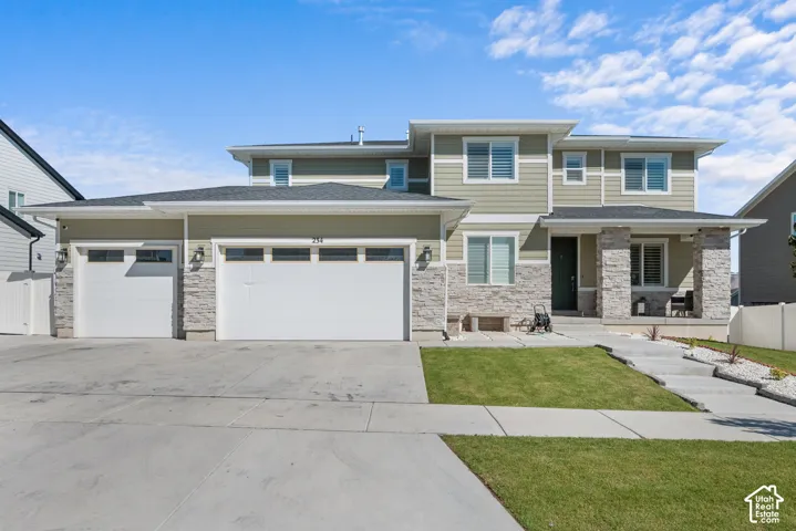 Contemporary two-story exterior featuring light green siding, stone accents, multiple windows with shutters, and a covered front porch with stone pillars