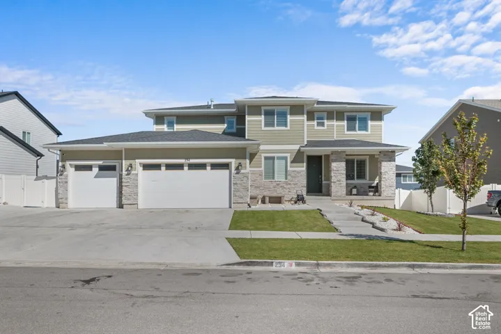 Two-story exterior with light green siding and stone accents, featuring a multi-car garage, covered porch, and landscaped front yard