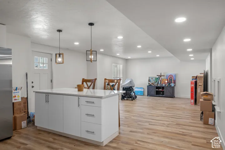 Open-concept interior featuring wood-finish flooring, recessed lighting, and a white kitchen island with a light-colored countertop