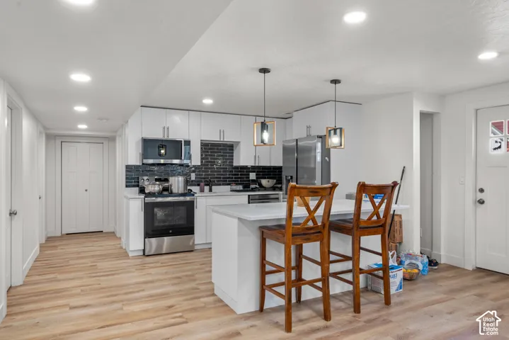 Kitchen with stainless steel appliances, white cabinetry, dark subway tile backsplash, recessed lighting, and wood-finish flooring