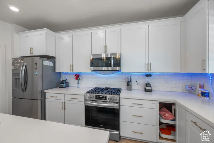 White shaker-style cabinetry with gold-tone hardware, stainless steel appliances, solid surface countertops, and white subway tile backsplash