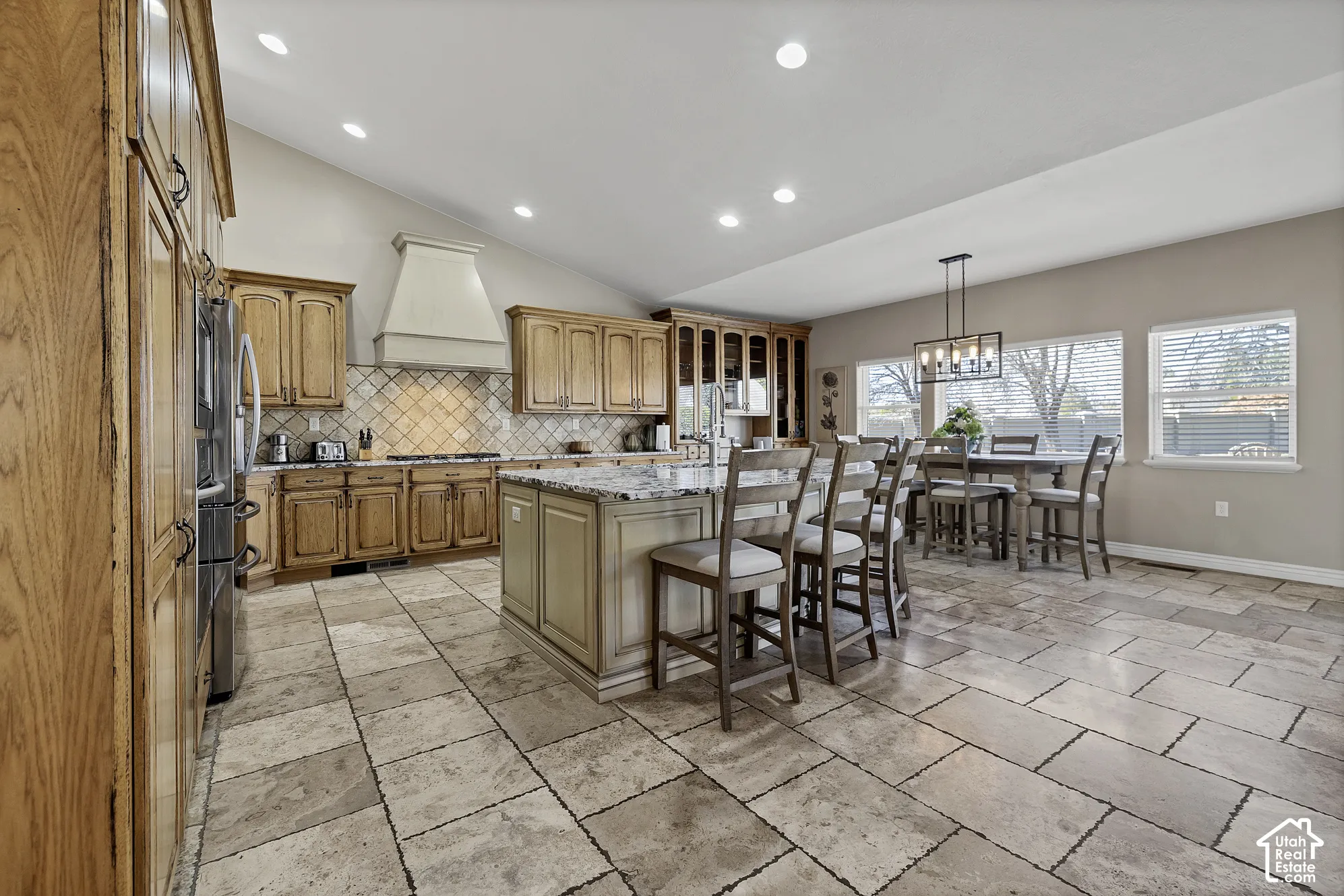 Spacious kitchen featuring an island with stone countertop, tile flooring, wood cabinetry, vaulted ceiling, and recessed lighting