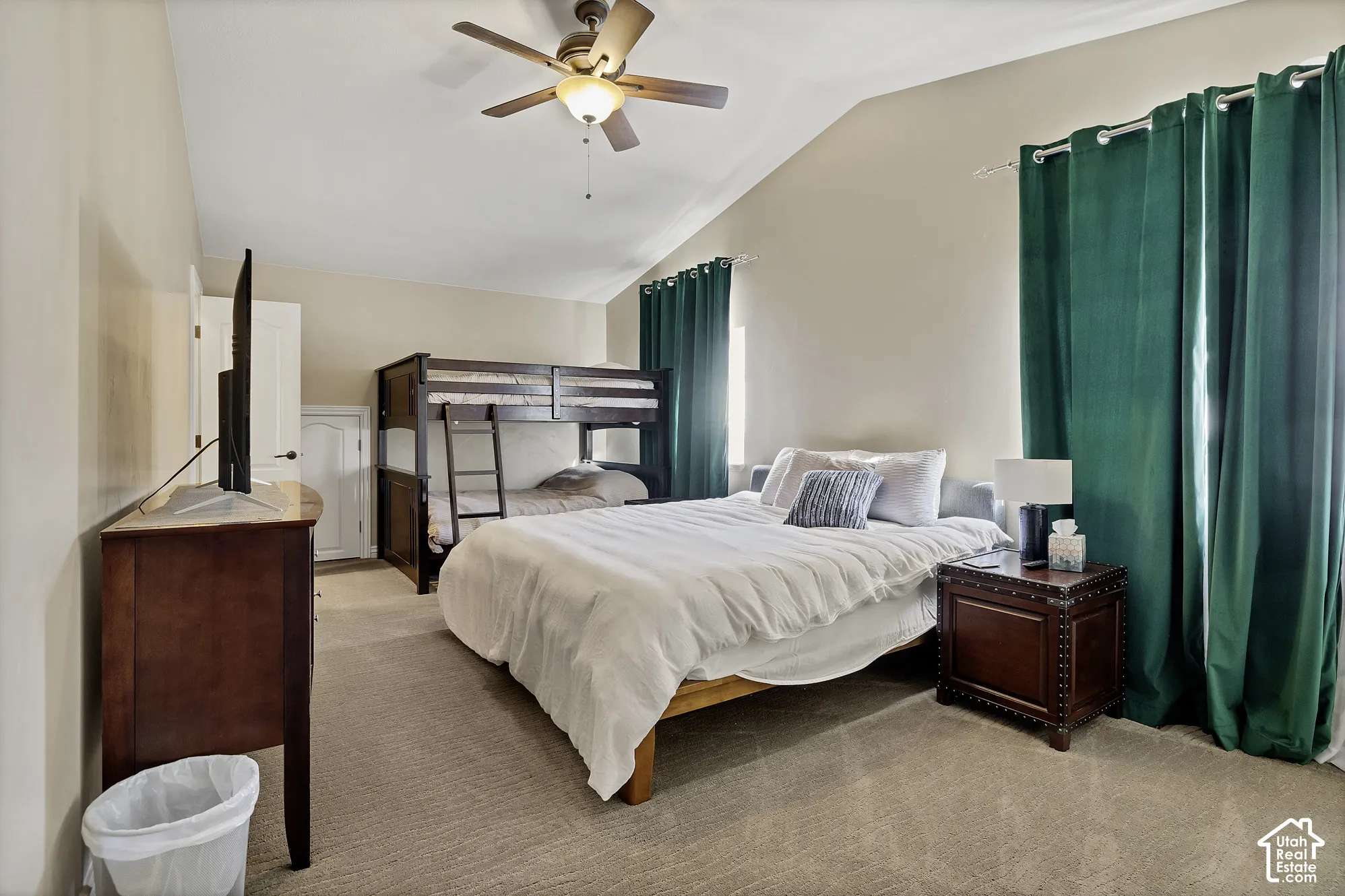 Vaulted ceiling, ceiling fan with integrated lighting, carpeted flooring, and privacy window treatments