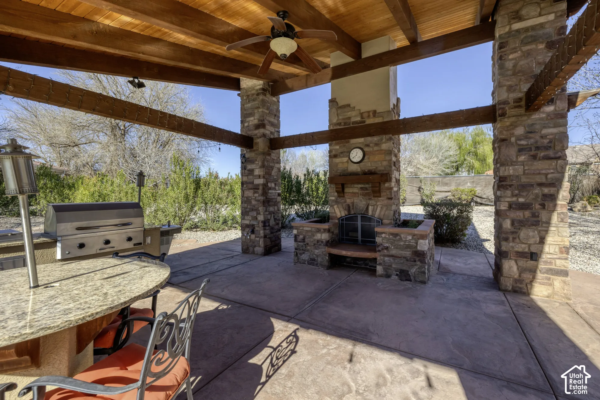 Covered patio with a wood-beamed ceiling, stone-clad columns, outdoor fireplace, and built-in grill