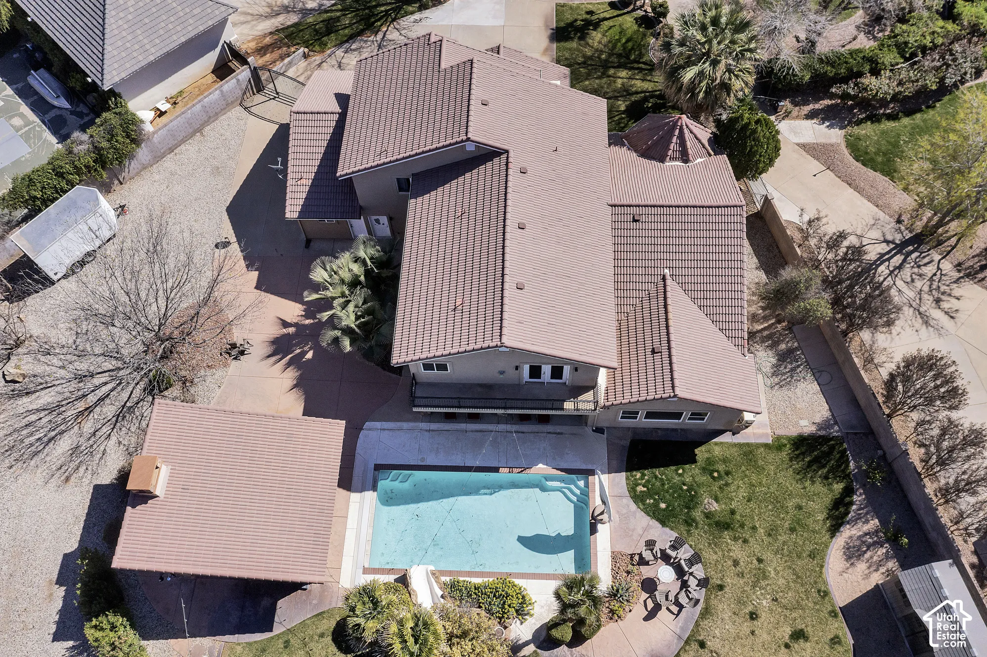 Aerial view showcasing a resort-style backyard oasis featuring a sparkling turquoise swimming pool, expansive covered patio with corrugated metal roofing, and mature landscaping throughout the grounds