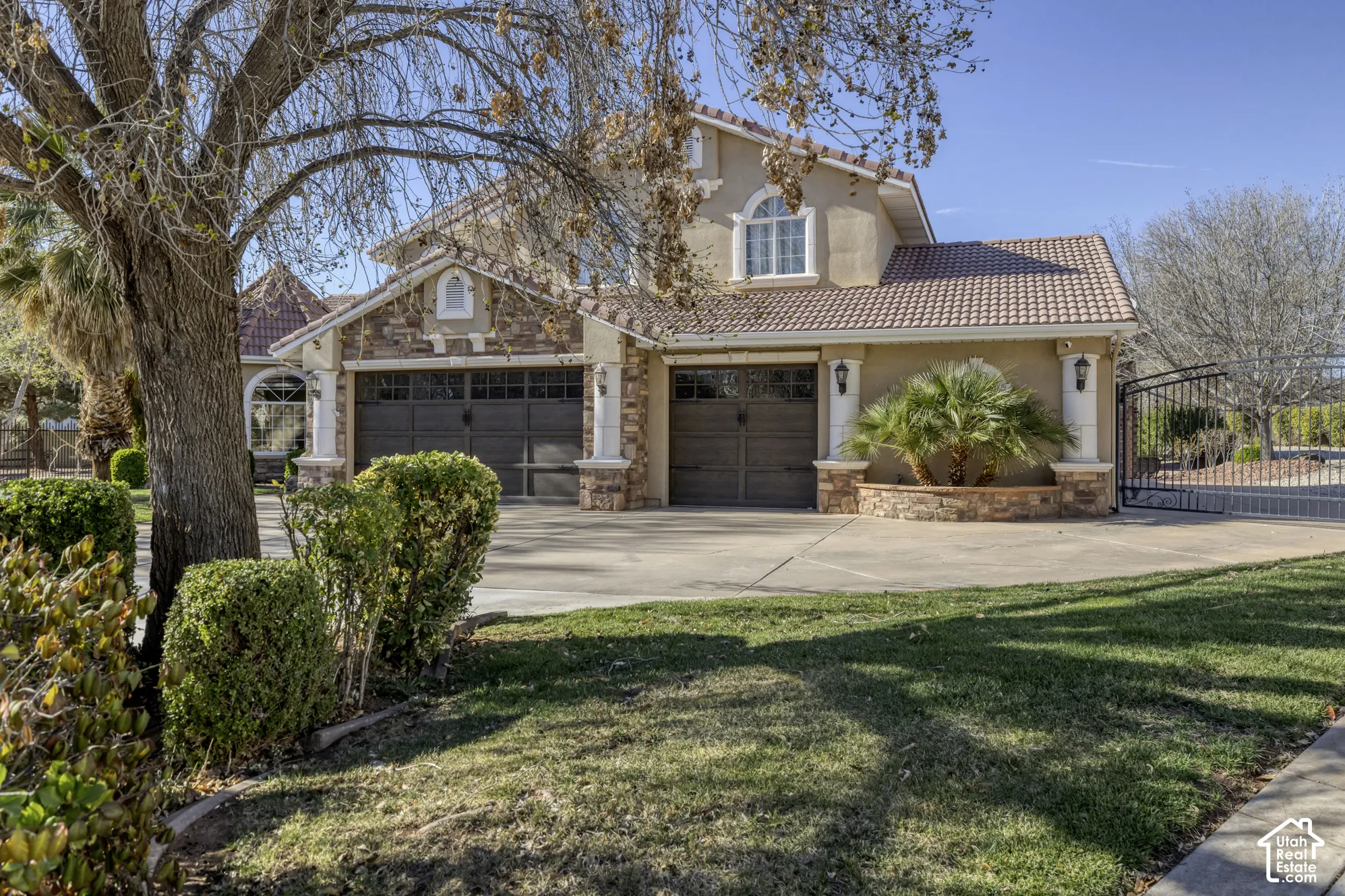 Stucco and stone exterior with a tile roof, featuring a multi-car garage, arched window, and wrought iron gate