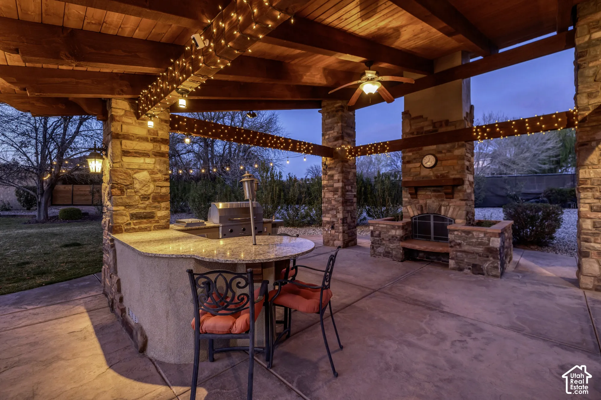Expansive outdoor living area featuring a stone fireplace, built-in outdoor kitchen with grill, wood beam patio cover, and stamped concrete patio