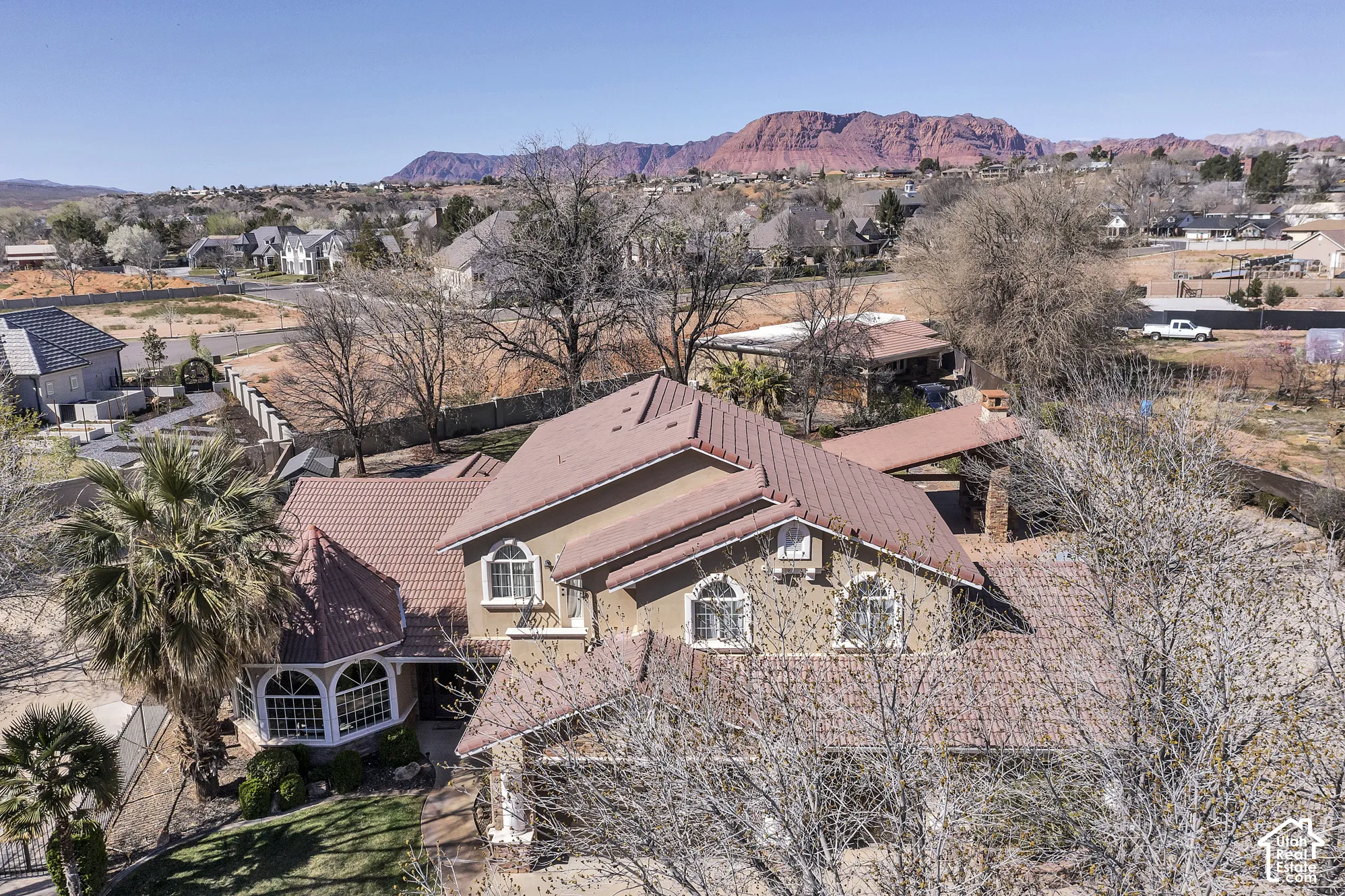 Terracotta tile roofing, stucco exterior, arched windows, covered outdoor structure, and mature palm trees