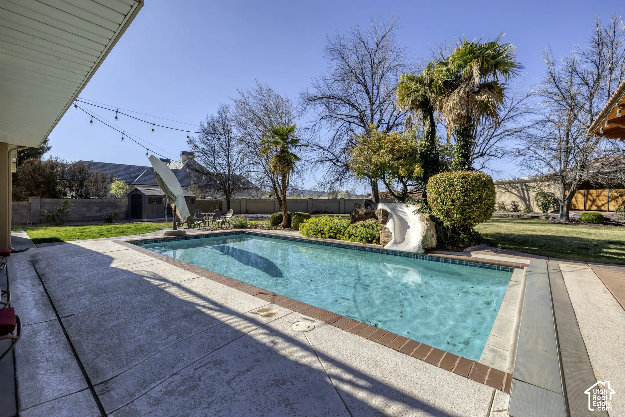 Swimming pool with a slide, surrounded by a concrete patio and established landscaping