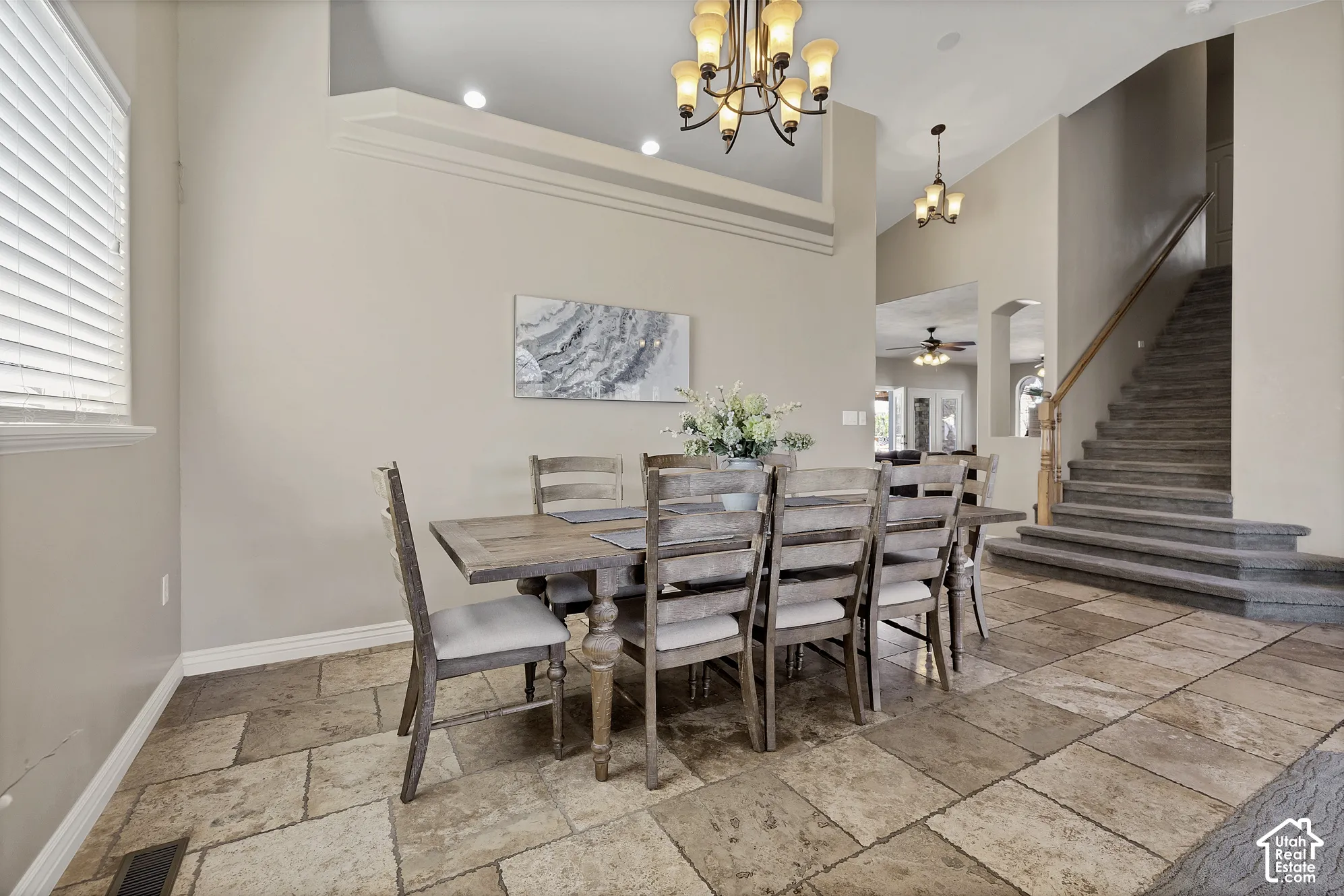 Expansive dining area featuring large-format tile flooring, a tiered chandelier, and a carpeted staircase with a wood handrail