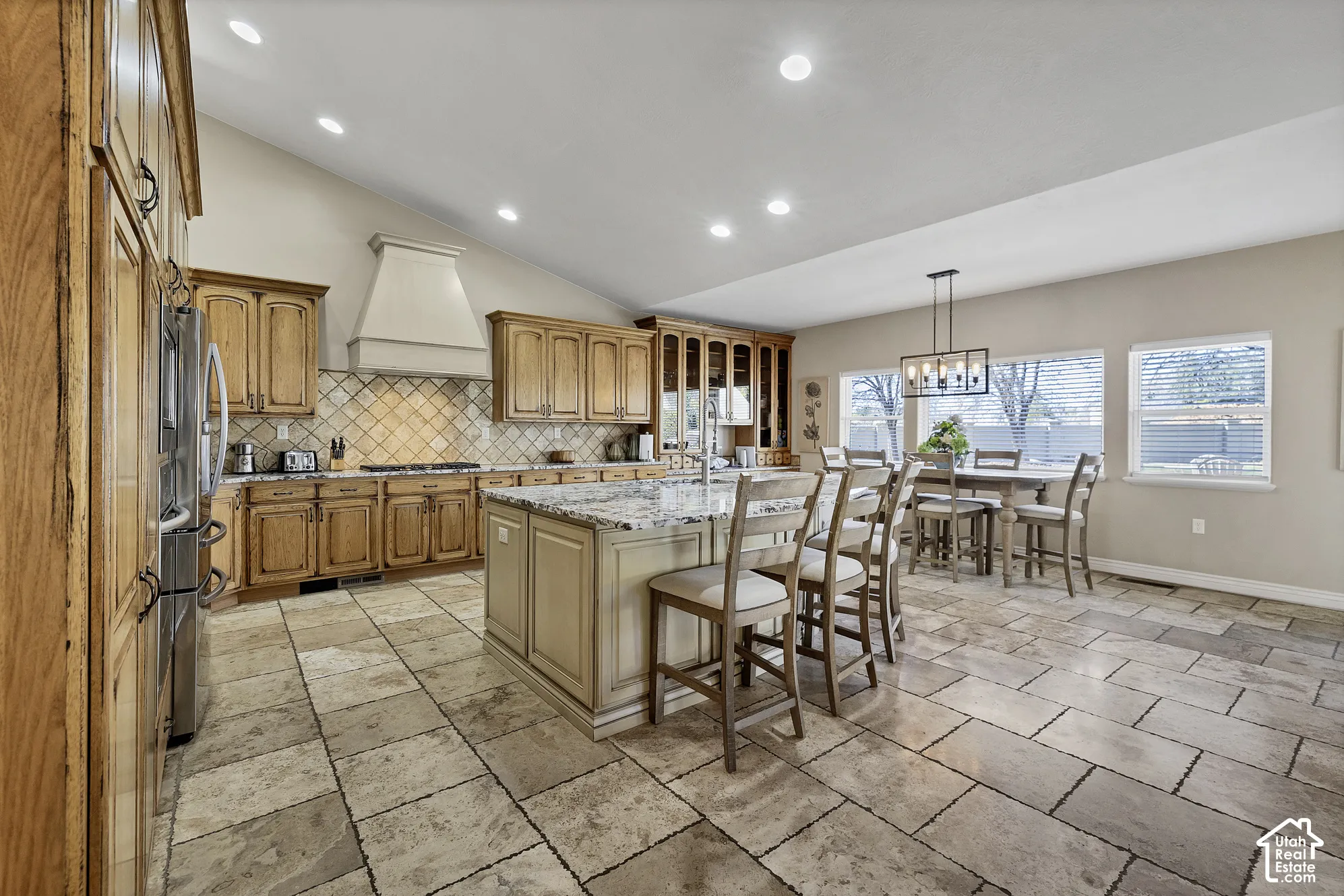 Vaulted ceiling kitchen featuring wood cabinetry, stone tile flooring, a center island with countertop seating, and recessed lighting