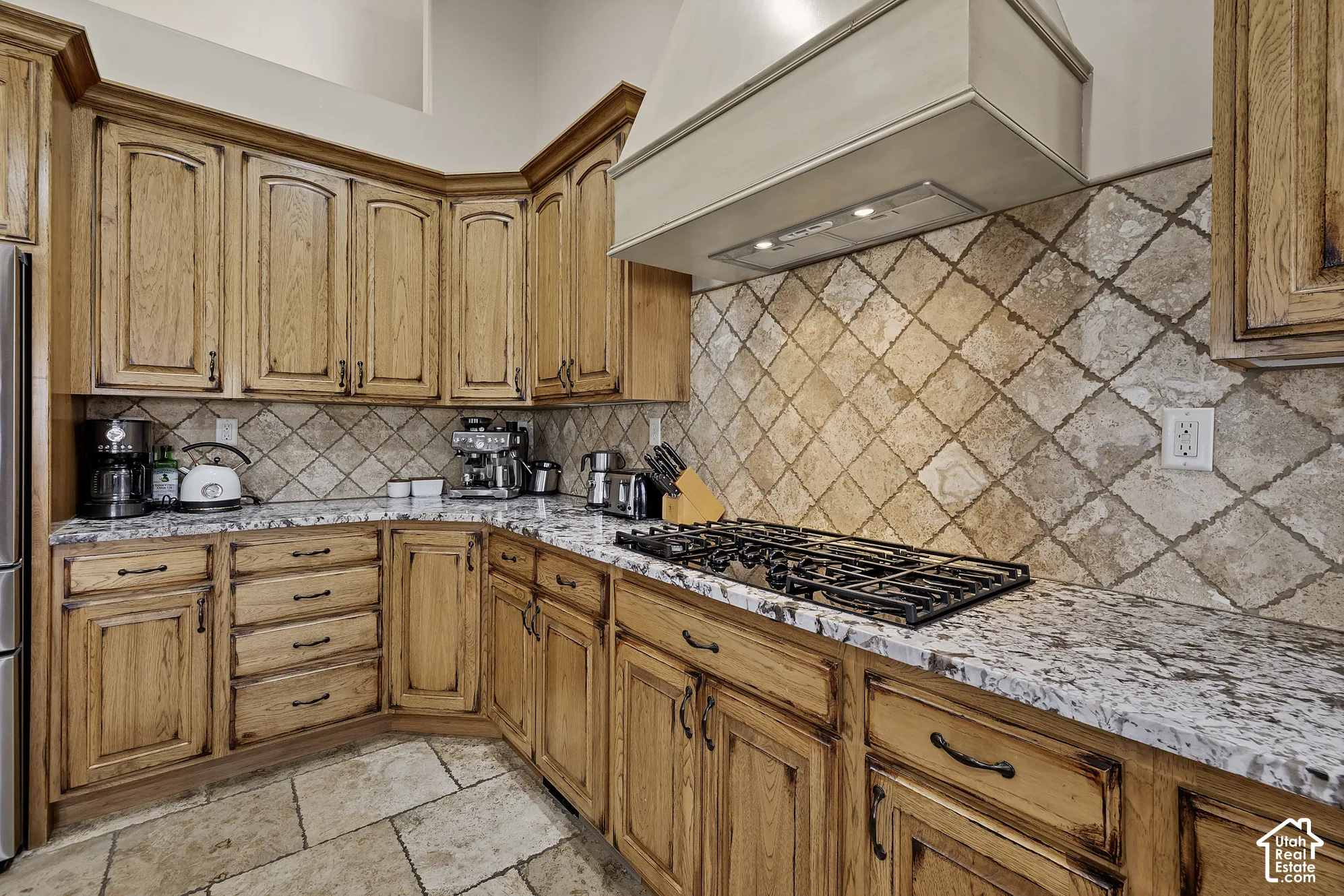 Kitchen featuring wood cabinetry, a tiled backsplash, stone countertops, a built-in gas range, and tile flooring