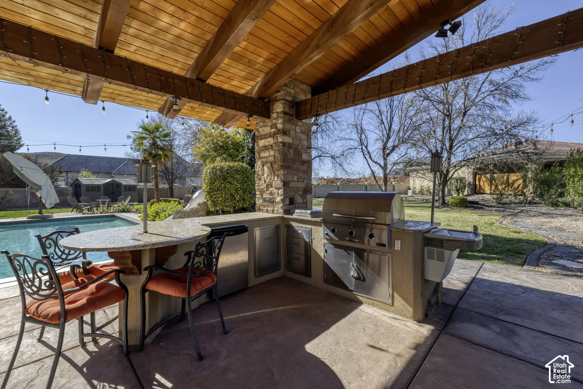 Outdoor kitchen featuring a built-in grill, stone-clad pillar, and a wood-beamed ceiling