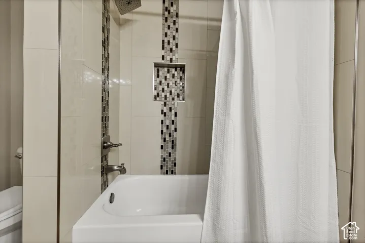 Bathtub with brushed nickel fixtures, a built-in shower niche, and mosaic tile accents