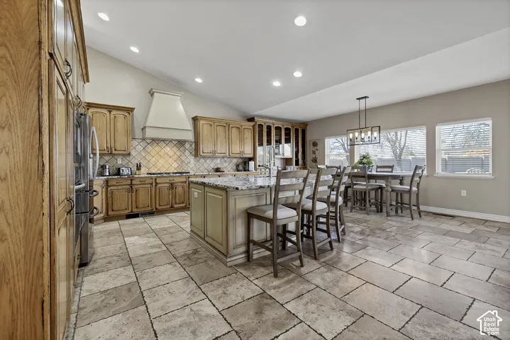 Spacious kitchen featuring an island with stone countertop, tile flooring, wood cabinetry, vaulted ceiling, and recessed lighting