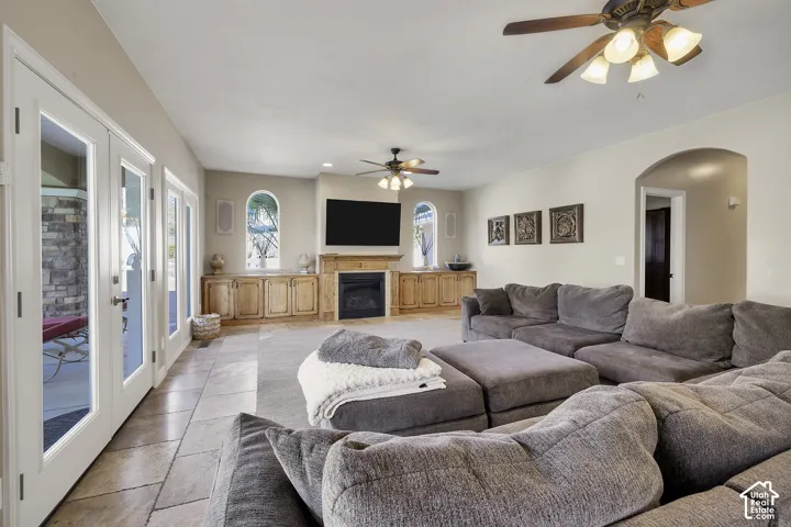 Spacious living area featuring tile flooring, built-in wood cabinetry with fireplace, ceiling fans with integrated lighting, arched architectural details, and French doors providing access to the exterior