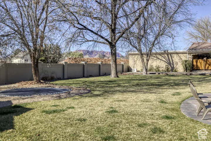 Expansive grassy yard with mature trees, a built-in trampoline, and a concrete patio