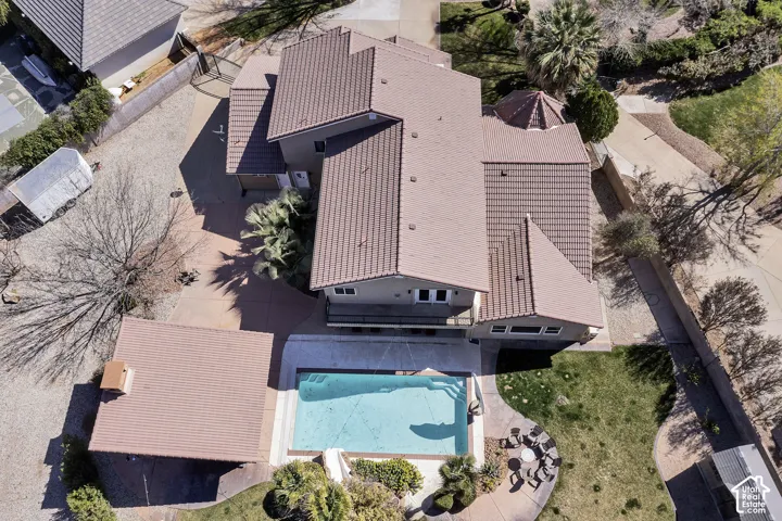 Aerial view showcasing a resort-style backyard oasis featuring a sparkling turquoise swimming pool, expansive covered patio with corrugated metal roofing, and mature landscaping throughout the grounds