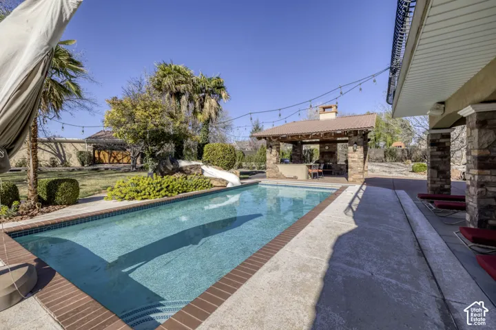 Outdoor swimming pool with brick coping, an adjacent covered patio, and a stone-clad outdoor kitchen