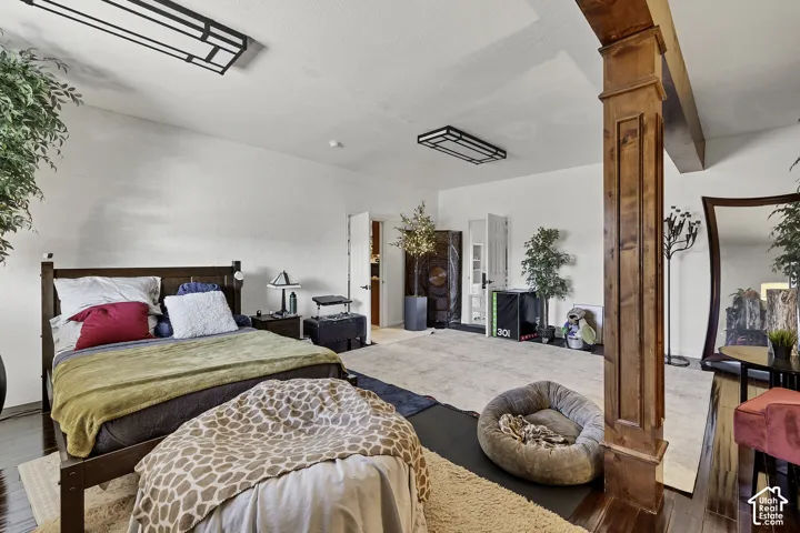 Spacious room featuring wood-finish flooring, white walls, and a prominent wood structural beam