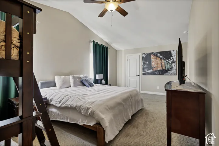 Vaulted ceiling with a ceiling fan, light-toned carpeting, and a white interior door