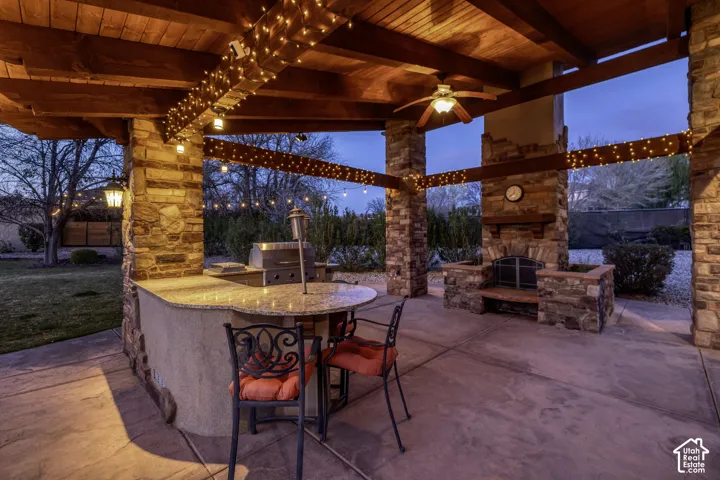 Expansive outdoor living area featuring a stone fireplace, built-in outdoor kitchen with grill, wood beam patio cover, and stamped concrete patio