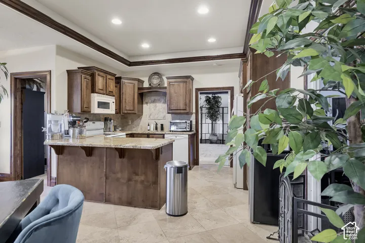 Kitchen featuring wood cabinetry, light-toned stone countertops, a matching stone backsplash, recessed lighting, and a kitchen island with corbel accents