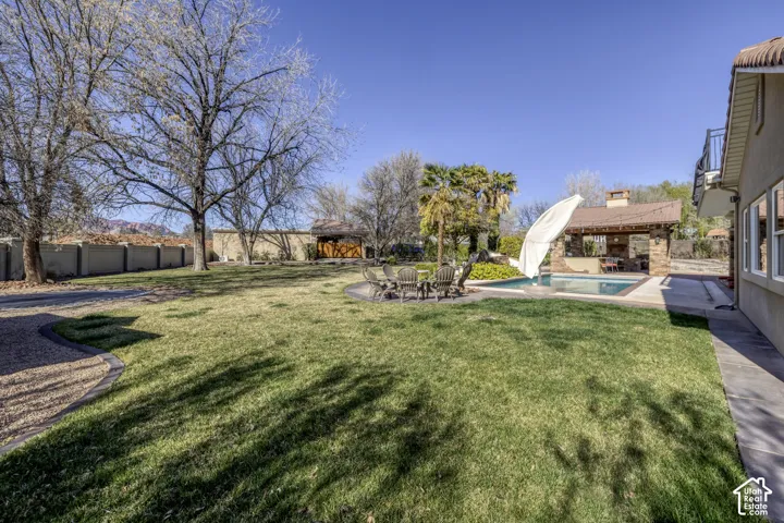 Expansive lawn area with a stone-surfaced outdoor kitchen, an in-ground swimming pool, and a gravel-edged pathway