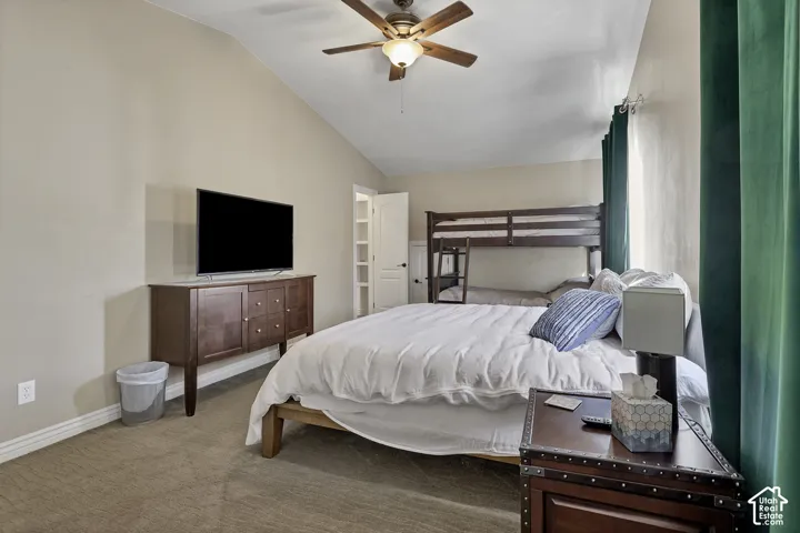 Vaulted ceiling with a ceiling fan, carpeted flooring, and a bunk bed