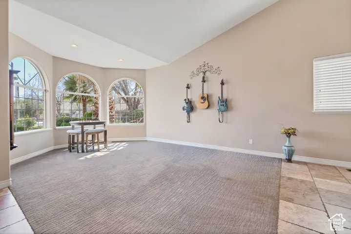 Multiple arched windows, vaulted ceiling, recessed lighting, and a blend of carpet and tile flooring