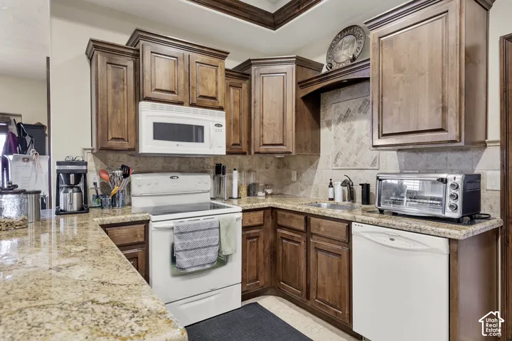 Kitchen featuring wood cabinetry, light-toned stone countertops, built-in microwave, and a tile backsplash