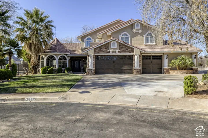 Stucco exterior with stone accents, arched windows, tile roof, three-car garage, and mature landscaping