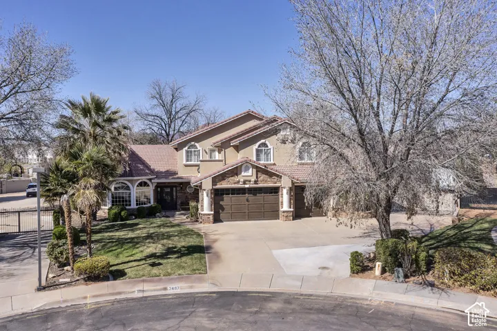 Stucco exterior with a tile roof, featuring an attached garage, arched windows, and mature landscaping
