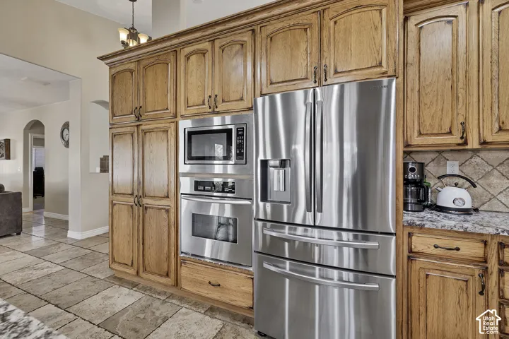 Wood-finish cabinetry with dark hardware, integrated stainless steel appliances, granite countertops, and tile flooring