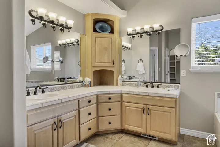 Dual vanity with light wood-finish cabinetry, tile countertops, and integrated sinks