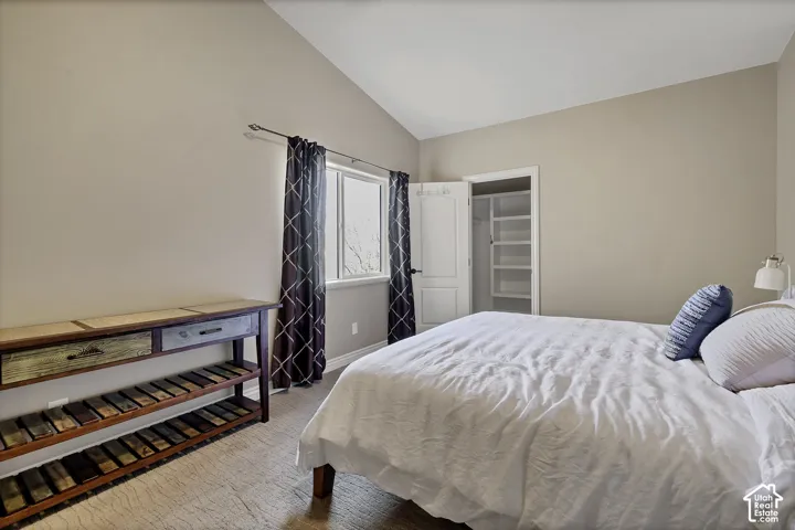 Vaulted ceiling, single window with trim, open closet with built-in shelving, carpet flooring