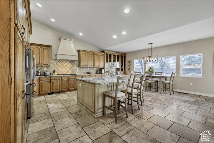 Vaulted ceiling kitchen featuring wood cabinetry, stone tile flooring, a center island with countertop seating, and recessed lighting