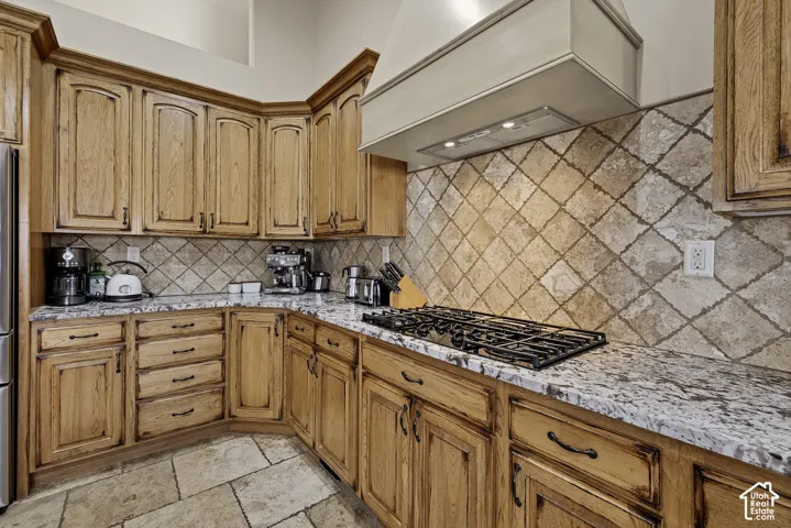 Kitchen featuring wood cabinetry, a tiled backsplash, stone countertops, a built-in gas range, and tile flooring