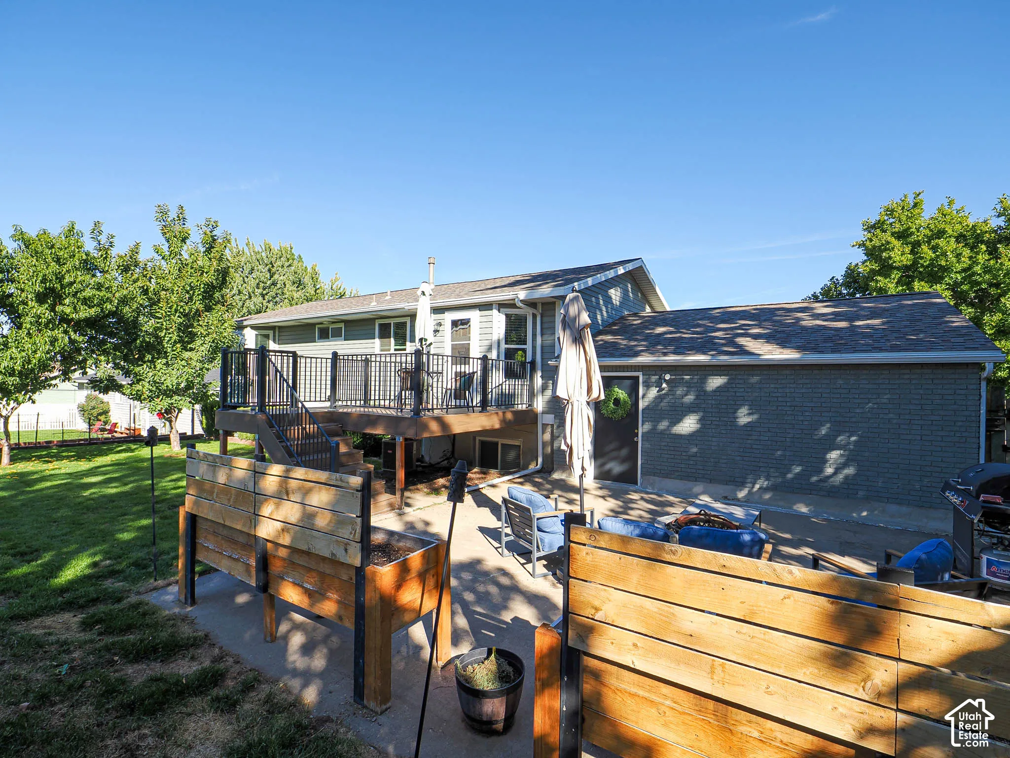 Expansive backyard featuring a multi-level deck with black railings, a ground-level concrete patio, and a separate structure with brick siding