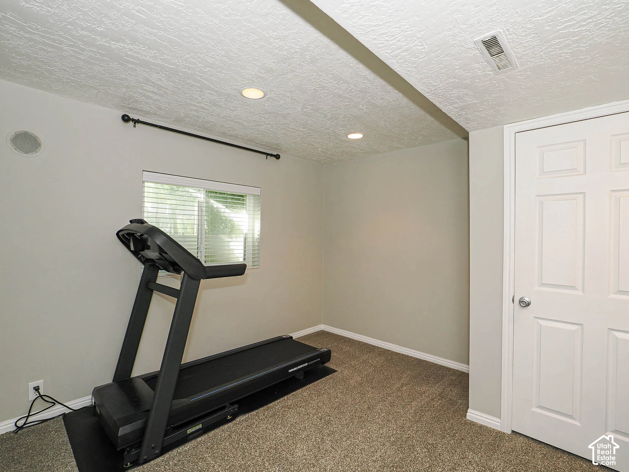 Recessed lighting, textured ceiling, light gray walls, carpet flooring, and a white paneled door