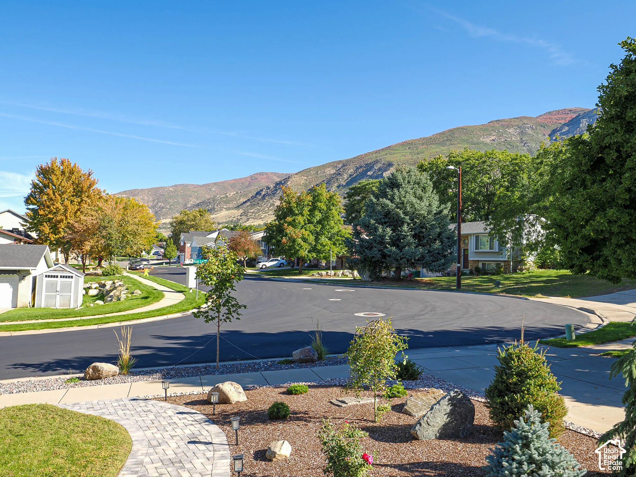 Decorative landscaping with a paver pathway, mature trees, and a mountain backdrop