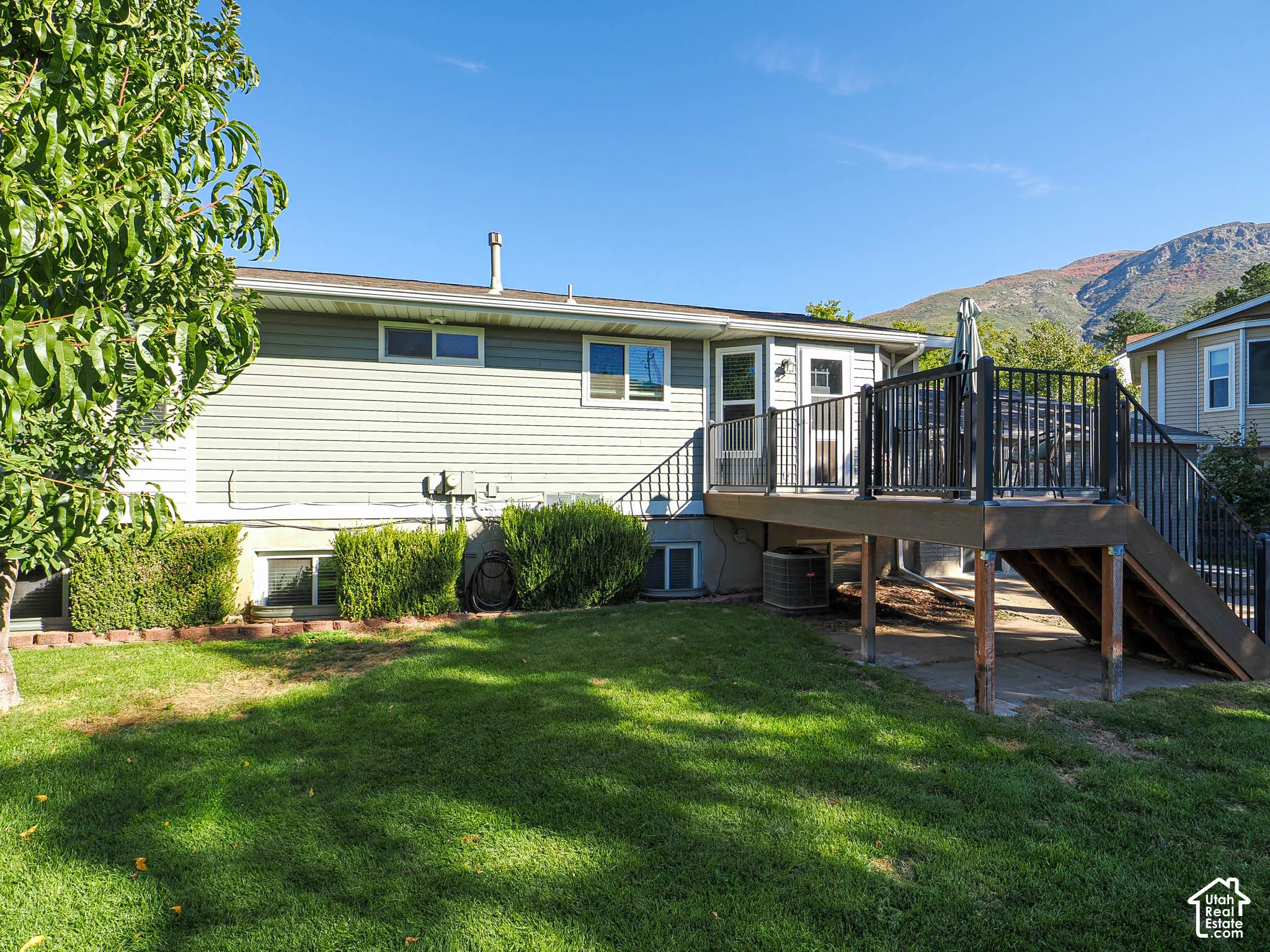 Expansive backyard featuring a multi-level deck with dark railing, mature landscaping, and a mountain backdrop