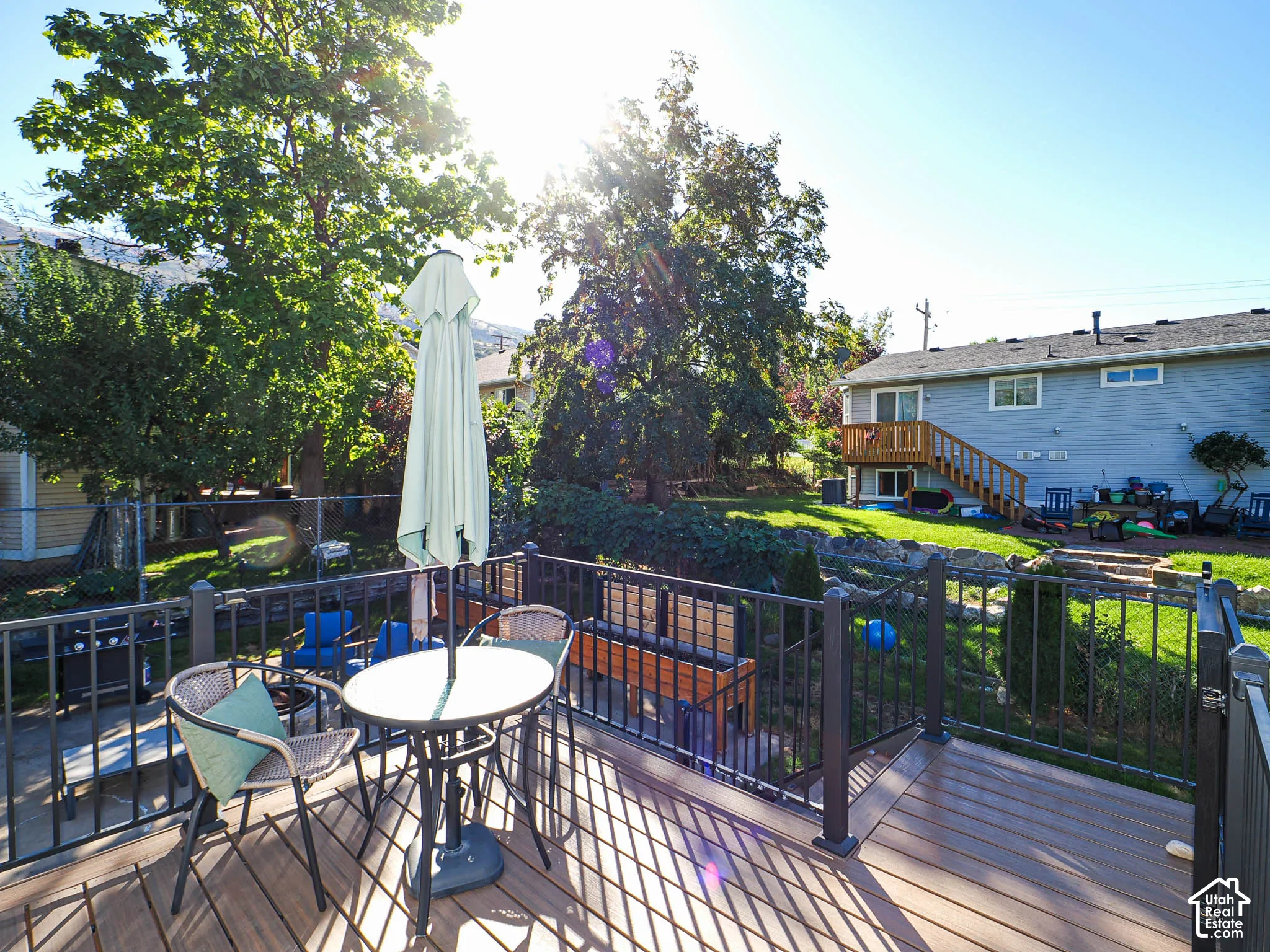Expansive deck with composite decking and dark railings, overlooking a tiered backyard with mature trees, established landscaping, and a chain link fence