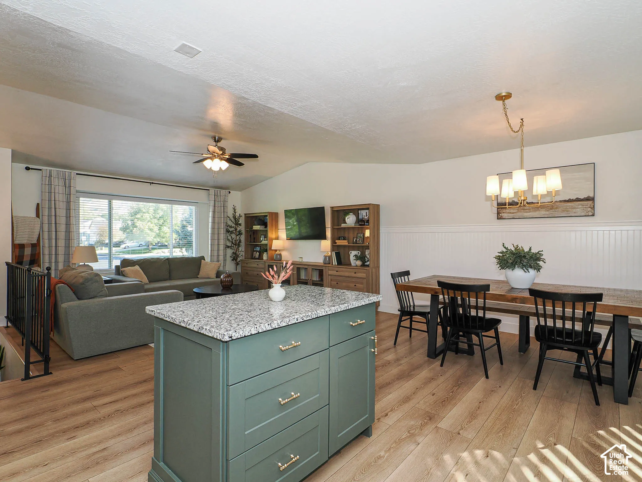 Expansive open-concept living space featuring wood-finish flooring, a vaulted ceiling, and a central island with a stone countertop