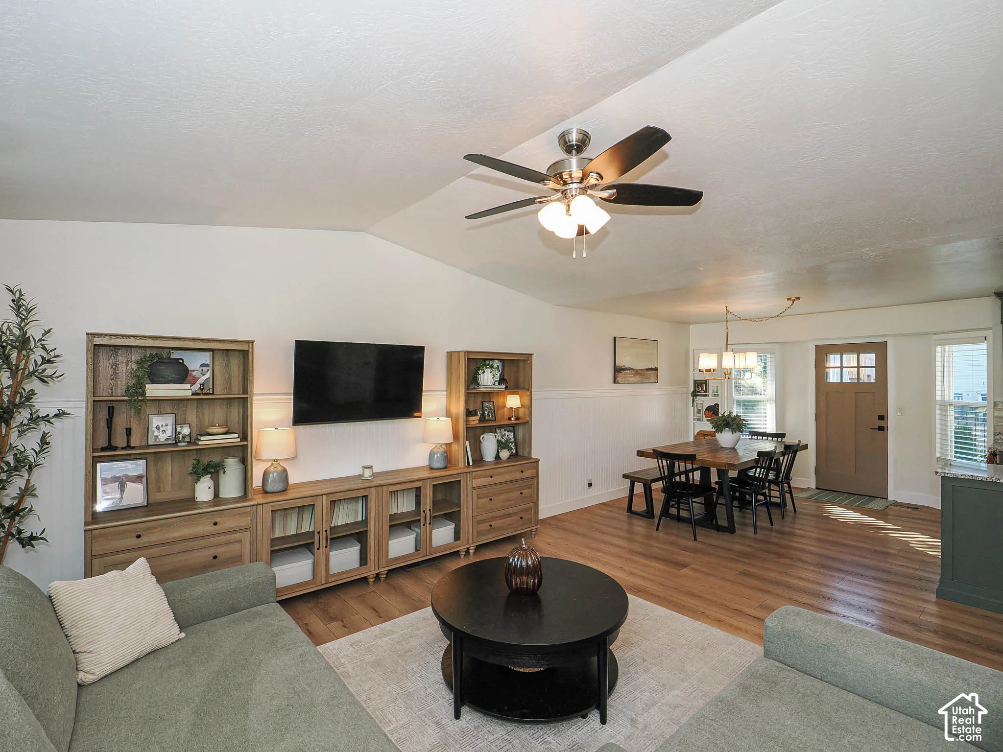 Vaulted ceiling with ceiling fan, wood-finish flooring, wainscoting, and a wood-panel entry door
