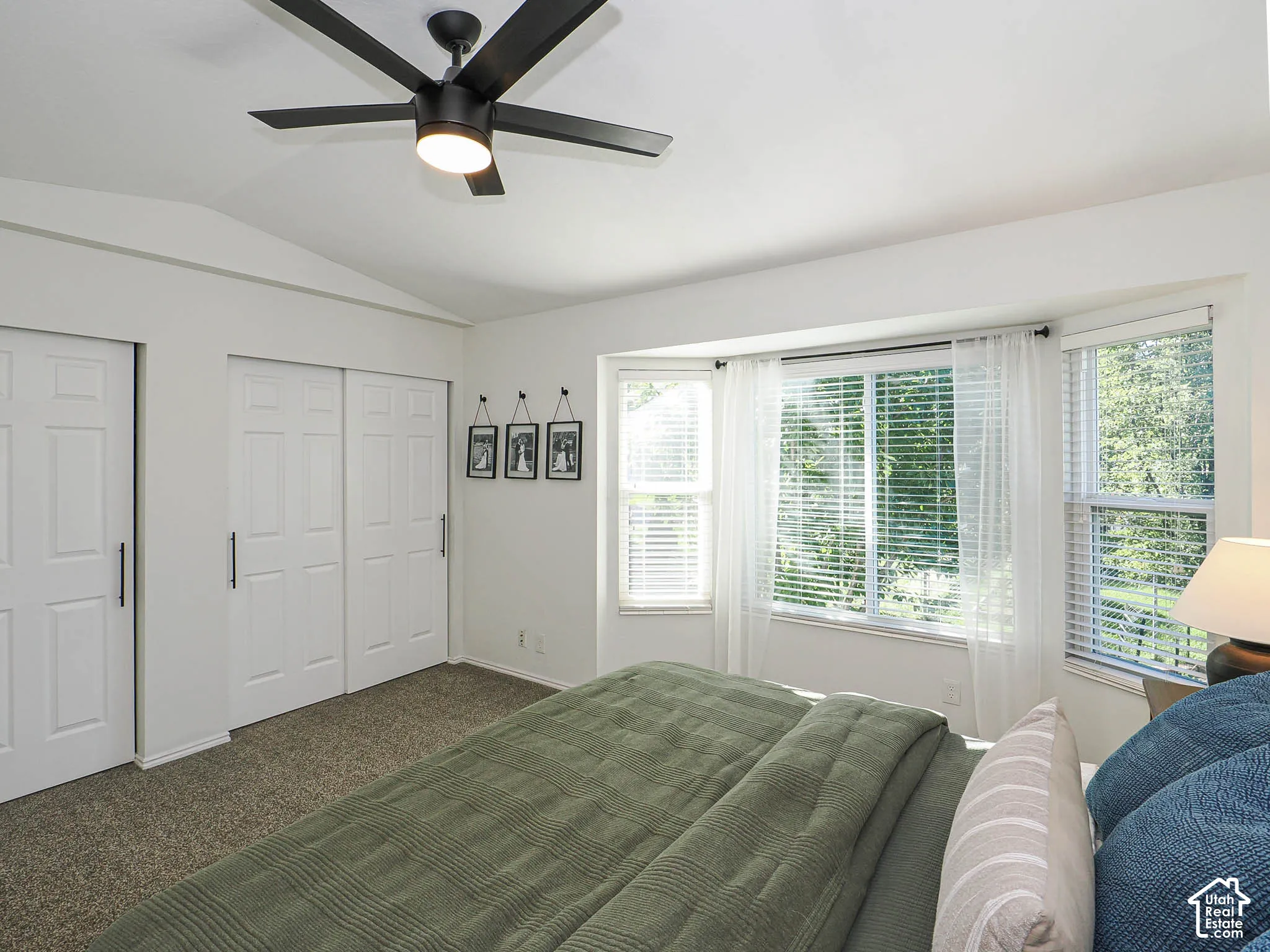 Vaulted ceiling with a black ceiling fan, white paneled closet doors, and multiple windows with white blinds