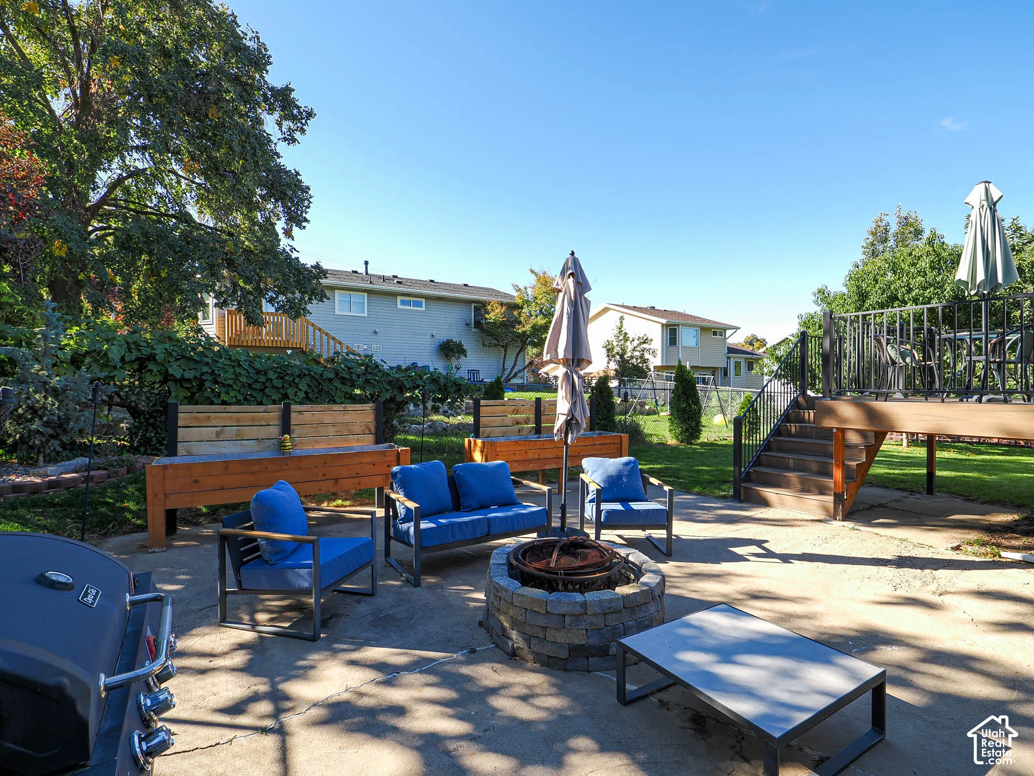 Expansive concrete patio featuring a stone fire pit, raised wood planters, and a multi-level wood deck with black metal railings