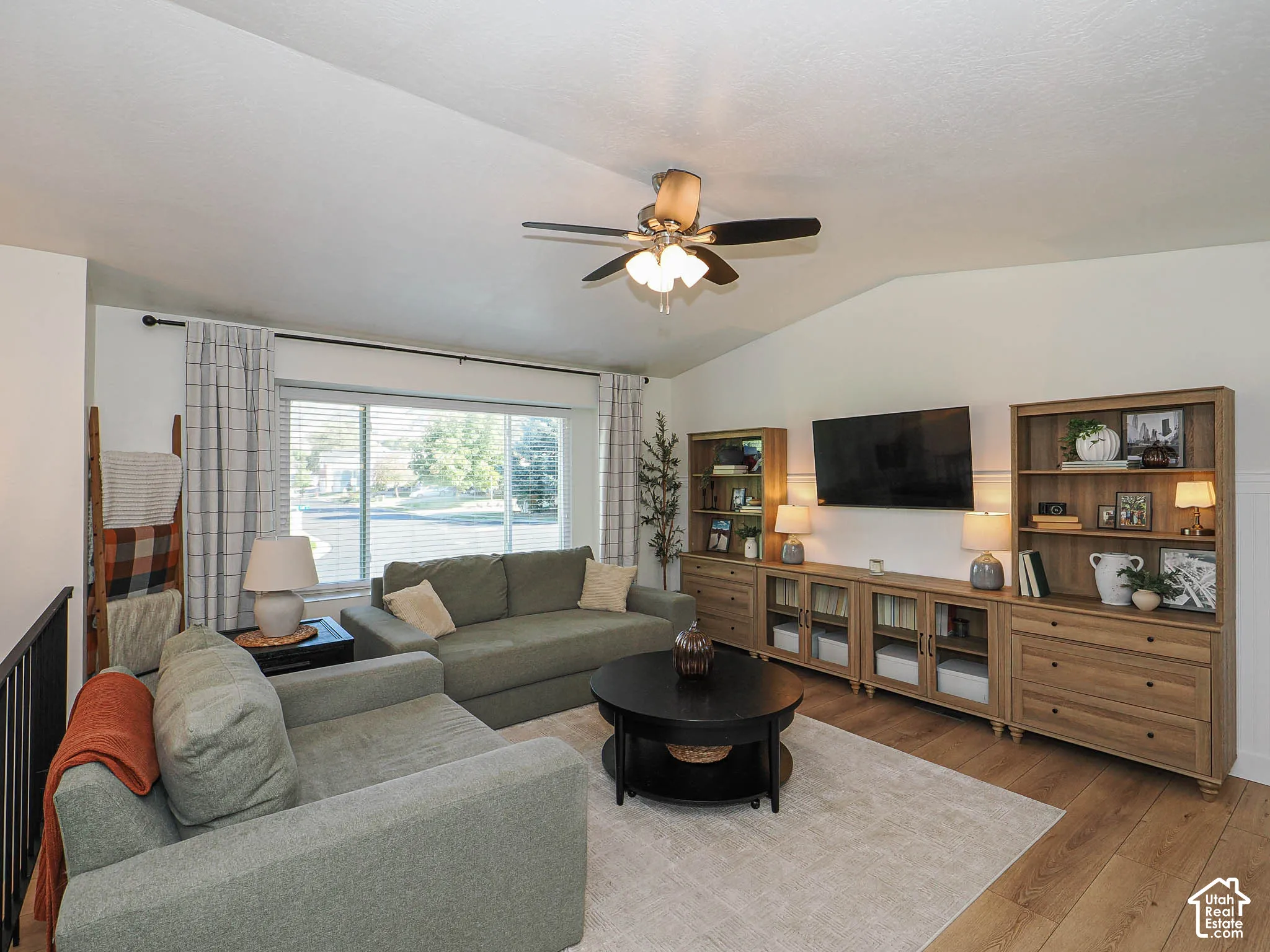 Vaulted ceiling, wood-finish flooring, ceiling fan with integrated lighting, expansive window, built-in entertainment center